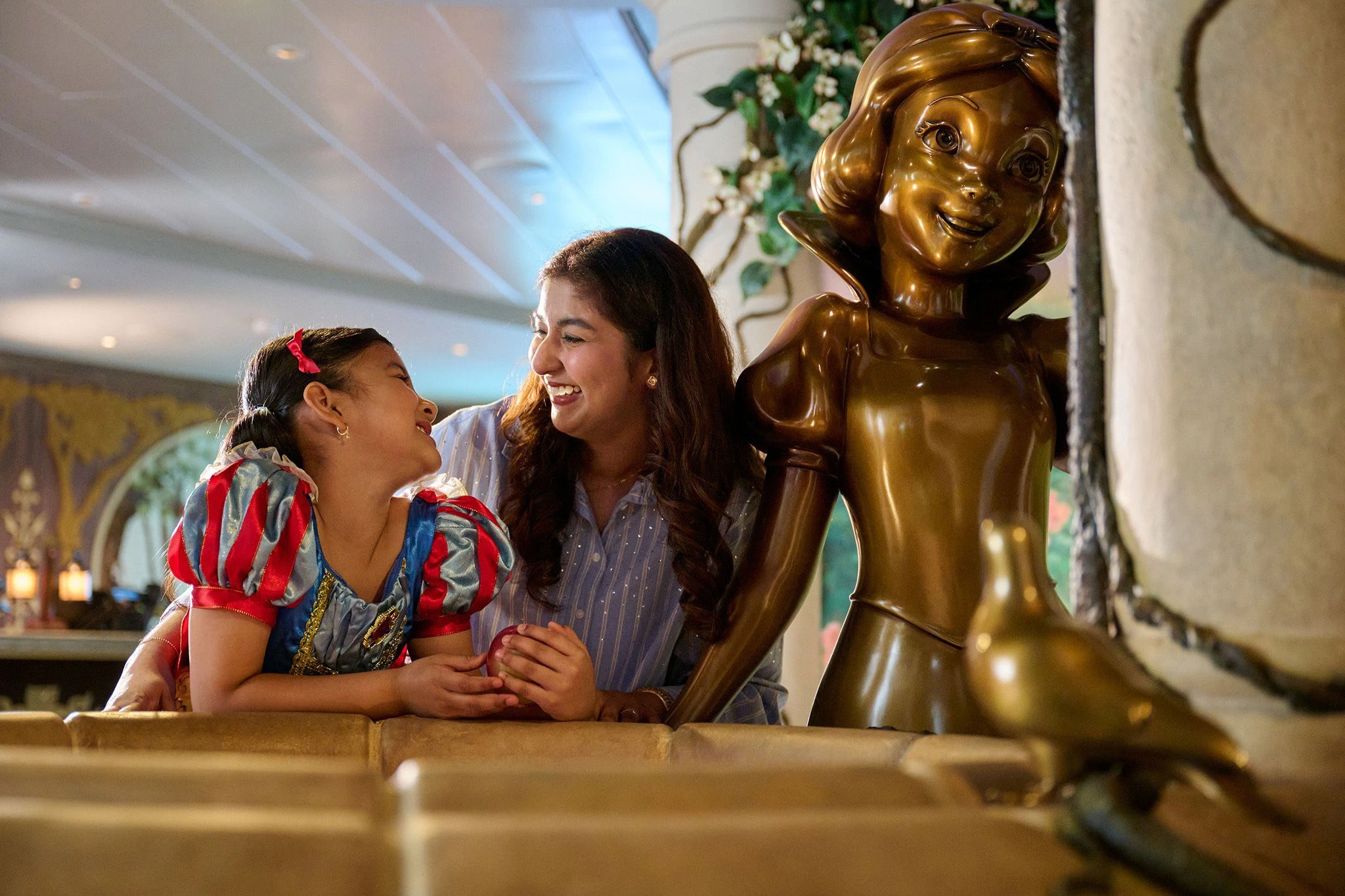 Mother and daughter in Snow White costume posing with golden Disney statue at Imagination Garden on Disney Adventure