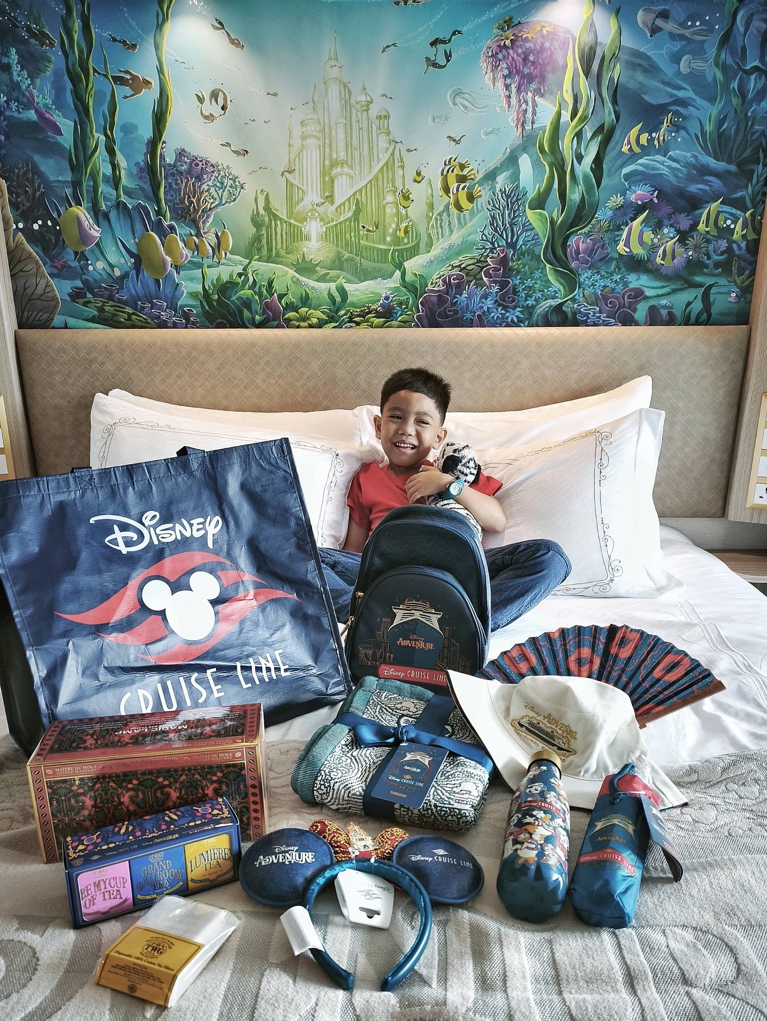 Child with Disney Cruise Line merchandise and souvenirs on stateroom bed with underwater mural on Disney Adventure