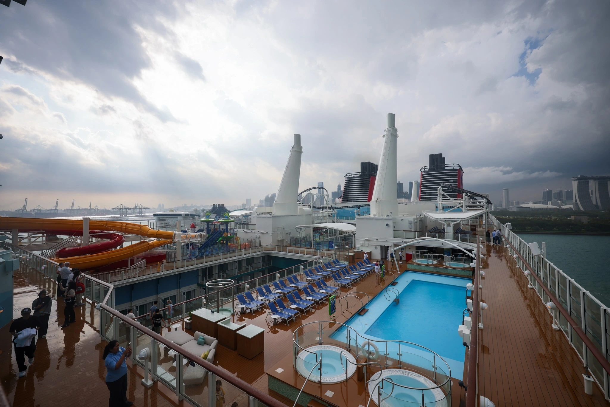 Disney Adventure upper deck panoramic view showing pool area hot tubs sun loungers funnels and Singapore skyline