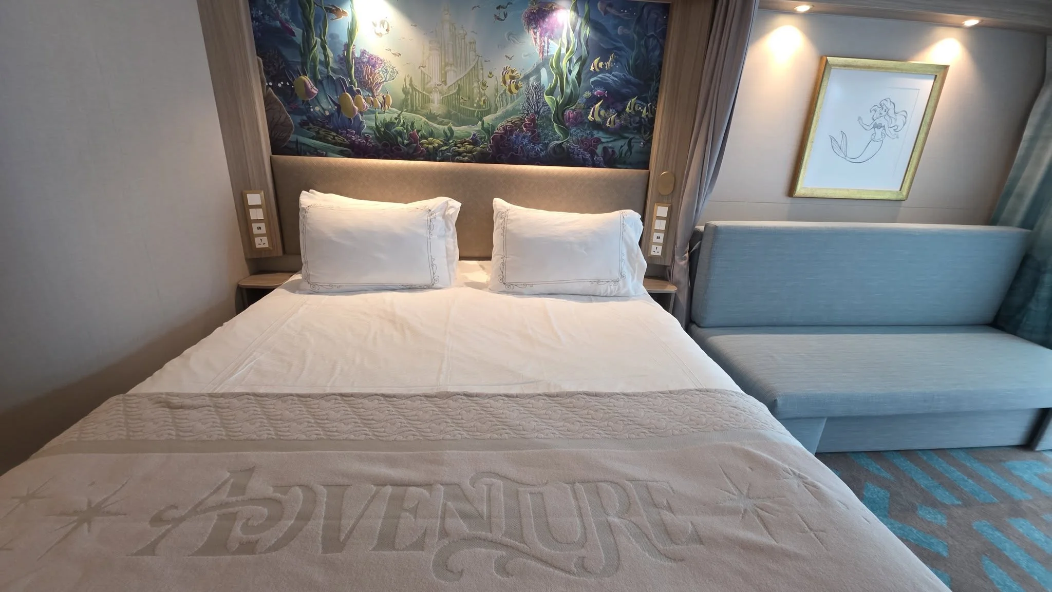 Disney Adventure stateroom bed closeup showing embroidered Adventure logo on white bedding with underwater headboard art