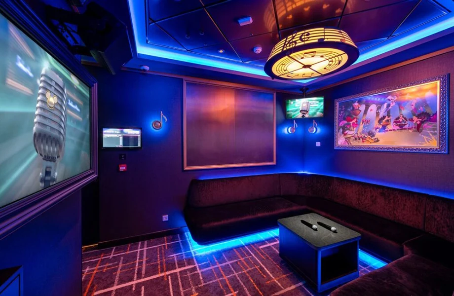 Private karaoke room at D-Lounge on the Disney Adventure — neon blue lighting, booth seating, and Disney villain artwork